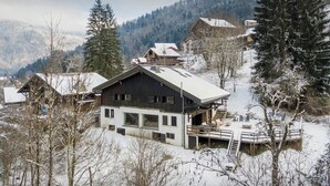 A modern two-story house with a balcony, surrounded by snow-covered trees and mountains in the background. - Chalet Fleur d'Aulps - Secluded holiday for 12 with spa - OVO Network (Saint-Jean-d'Aulps)