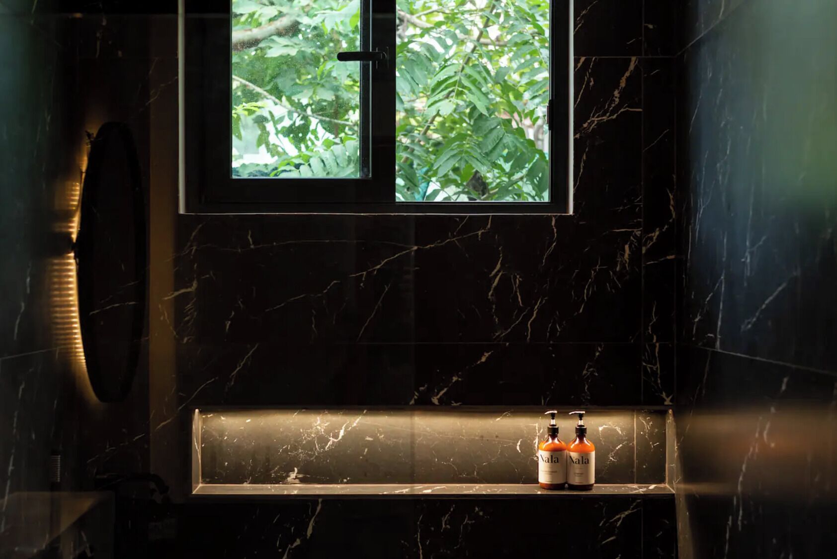 A bathroom with a marble sink, a window with a view of greenery, and two bottles labeled "Vala" on the counter.