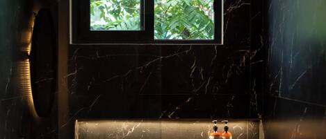 A bathroom with a marble sink, a window with a view of greenery, and two bottles labeled "Vala" on the counter.