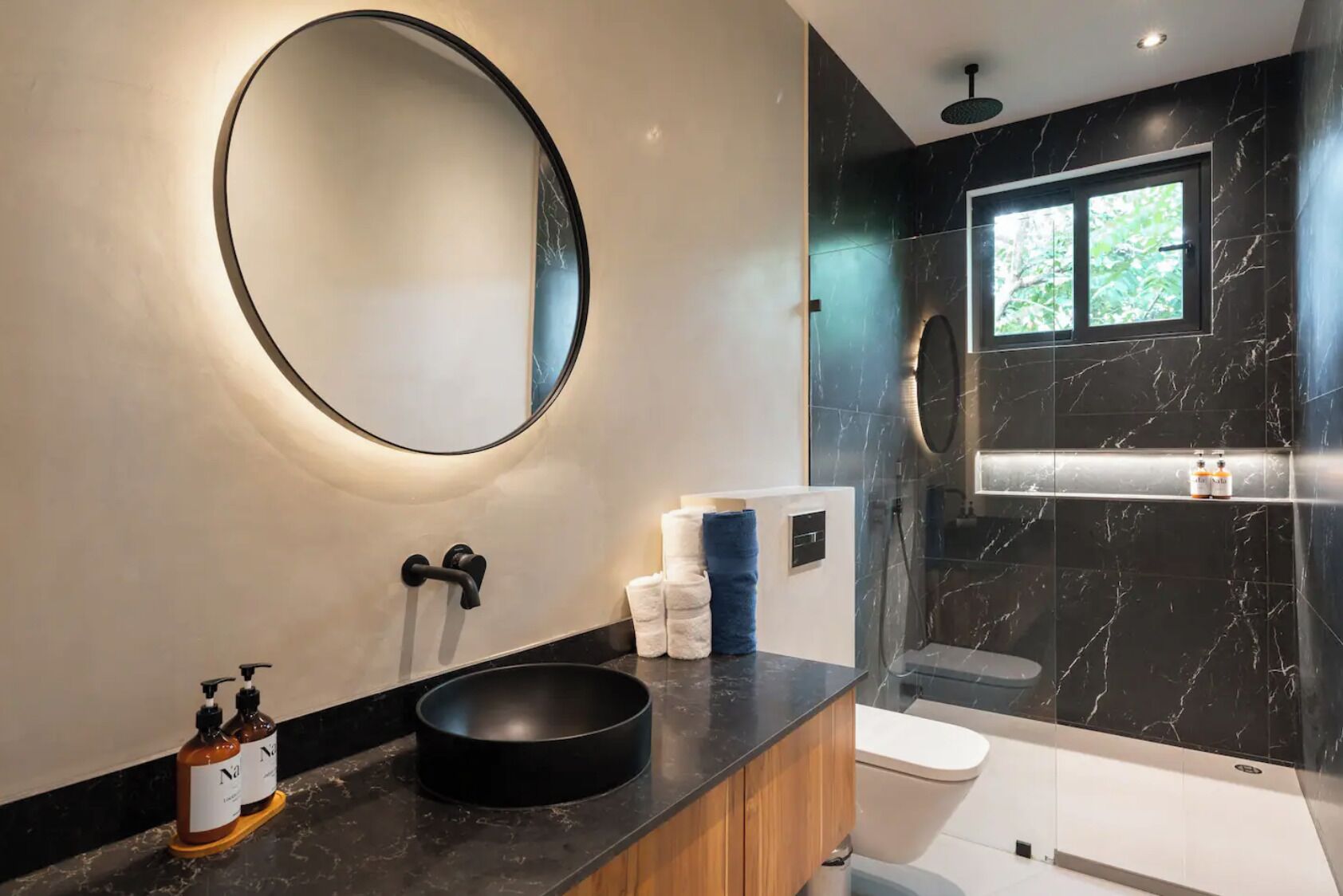 A modern bathroom with a round mirror, black sink, and marble walls.