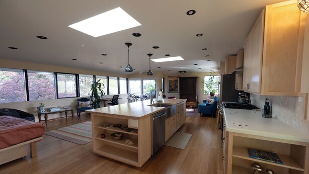 Una cocina amplia con armarios de madera, una isla central y un comedor con vistas a los cerezos en flor.