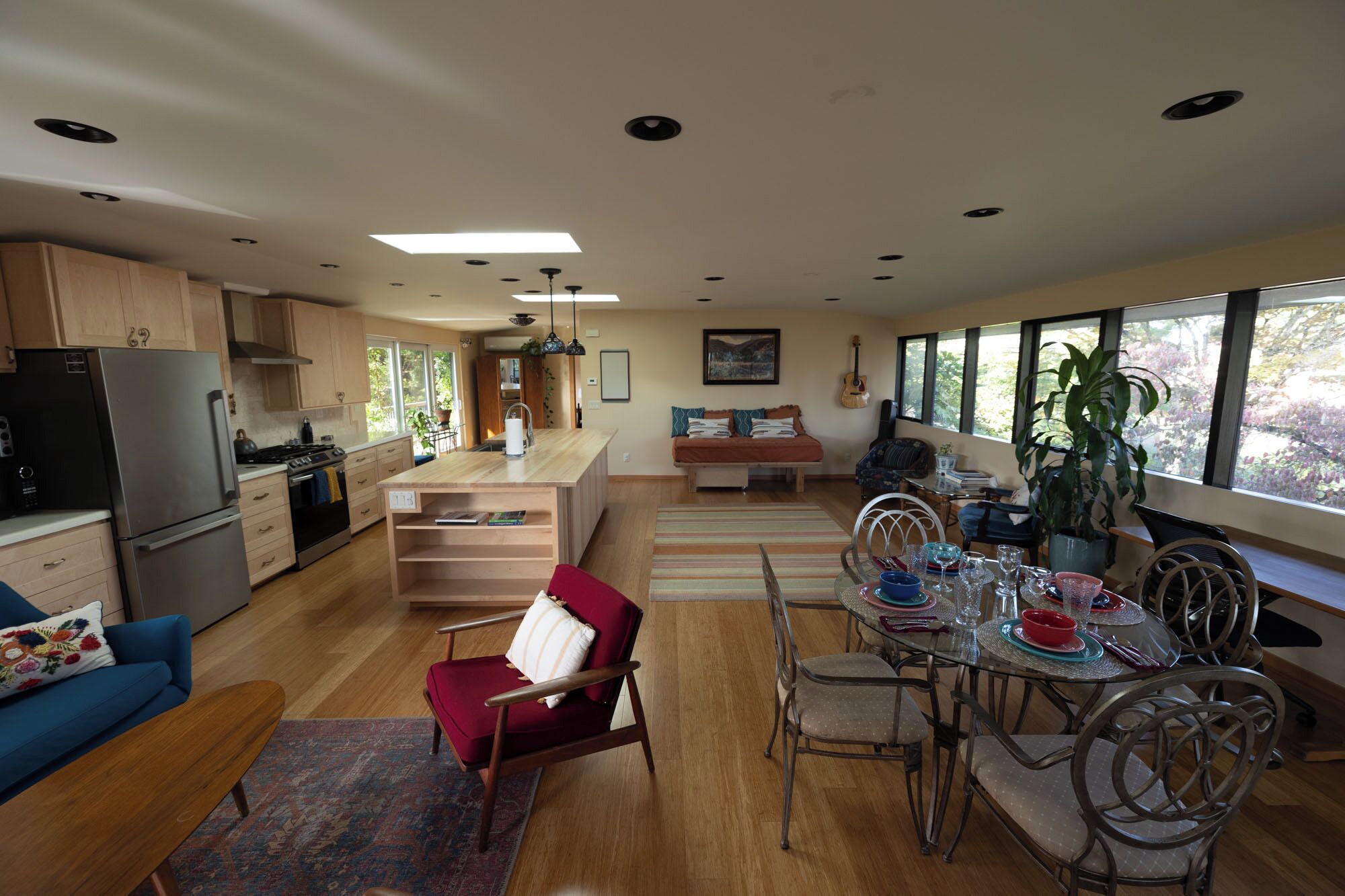 Una cocina moderna con una isla central, armarios de madera y una zona de comedor con mesa de vidrio y sillas metálicas.