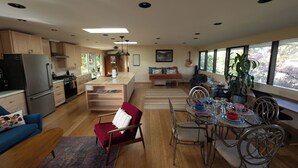 Una cocina moderna con una isla central, armarios de madera y una zona de comedor con mesa de vidrio y sillas metálicas.