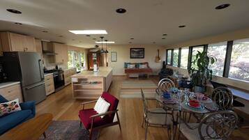 Una cocina moderna con una isla central, armarios de madera y una zona de comedor con mesa de vidrio y sillas metálicas.