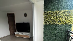 Una sala de estar moderna con un televisor de pantalla plana, un mueble de entretenimiento minimalista y una cerca artificial verde.