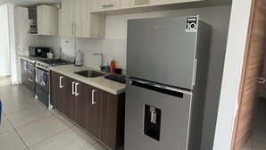 Una cocina moderna con electrodomésticos de acero inoxidable, armarios de madera clara y piso de baldosas.