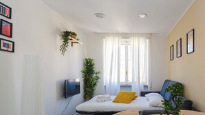 A modern hotel room with a bed, a TV, a desk with a chair, a potted plant, and a window with curtains. - Charming Apartment with AC, WiFi close to St. Peter’s Square, Roma. (Roma)