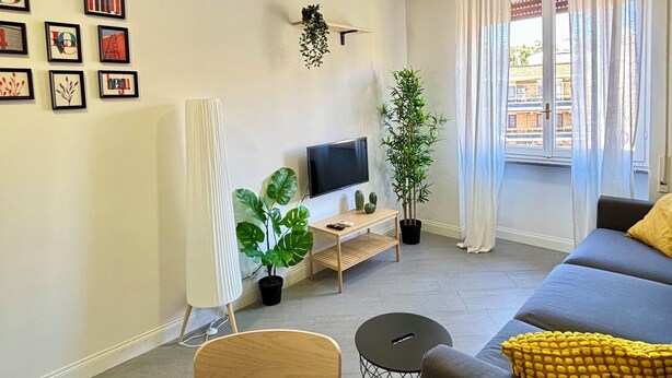 A modern living room with a sofa, a TV, a dining table, and various plants. - Charming Apartment with AC, WiFi close to St. Peter’s Square, Roma. (Roma)
