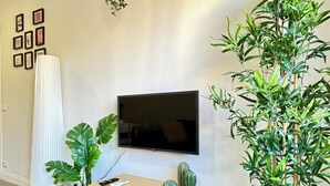 A modern living room with a flat-screen TV mounted on the wall, a wooden coffee table, and two potted plants. - Charming Apartment with AC, WiFi close to St. Peter’s Square, Roma. (Roma)