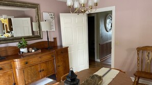 Comedor con una mesa de madera, sillas, una araña, un espejo y una puerta que da a una escalera.