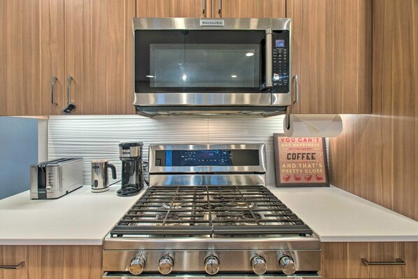 Una cocina moderna con un microondas de acero inoxidable, una estufa a gas, un tostador y una cafetera.
