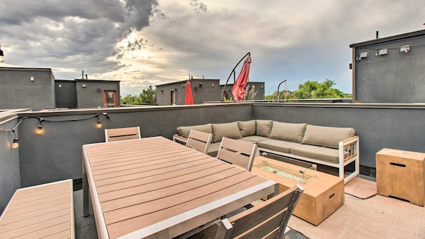 Um terraço no telhado com mesa e cadeiras de madeira, um sofá e um guarda-sol vermelho.
