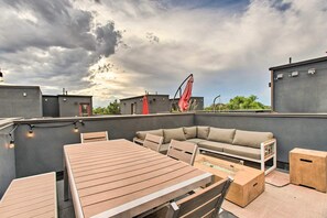 Una terraza en la azotea con una mesa y sillas de madera, un sofá y un paraguas rojo.