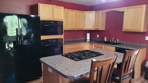 A kitchen with wooden cabinets, a black refrigerator, a built-in oven, a gas stove, and granite countertops.