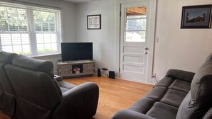 Una sala de estar con dos sofás de cuero, un televisor sobre un mueble de madera, una puerta y una ventana con persianas.