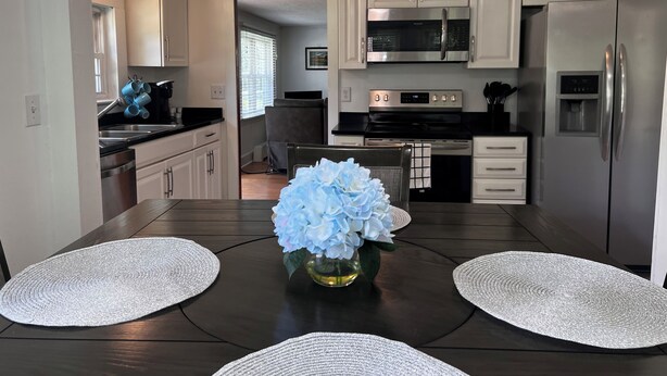 Una cocina moderna con electrodomésticos de acero inoxidable, armarios blancos y un comedor con una mesa lista para dos.