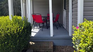 Un patio techado con una mesa y sillas, rodeado de follaje.