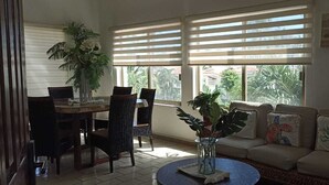 A living room with a sofa, a coffee table, a dining table with chairs, and large windows with blinds. - Beach Apartment with Swimming Pool and Tennis Court (Manzanillo)
