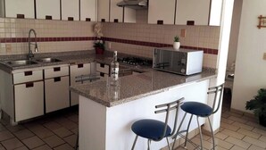 A kitchen with a central island, two bar stools, a microwave, and a sink. - Beach Apartment with Swimming Pool and Tennis Court (Manzanillo)
