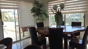 A dining area with a round table and chairs, a potted plant, and a view through a sliding glass door. - Beach Apartment with Swimming Pool and Tennis Court (Manzanillo)