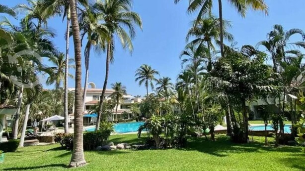 A resort with palm trees, a swimming pool, and a building with a white facade. - Beach Apartment with Swimming Pool and Tennis Court (Manzanillo)