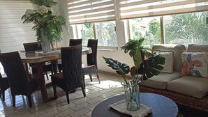 A room with a dining table, chairs, a sofa, and a round coffee table. There are potted plants and a window with blinds. - Beach Apartment with Swimming Pool and Tennis Court (Manzanillo)