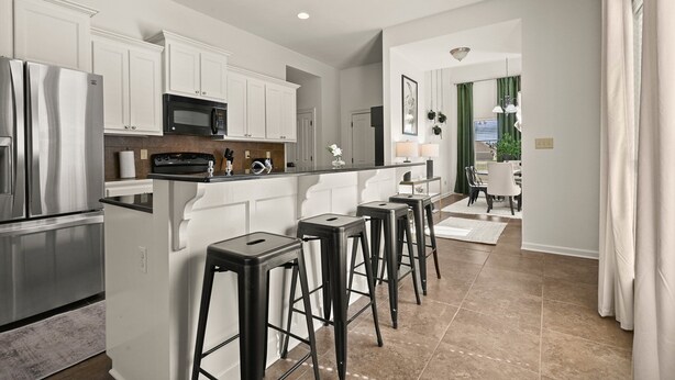 A modern kitchen with white cabinets, stainless steel appliances, and a bar area with stools.