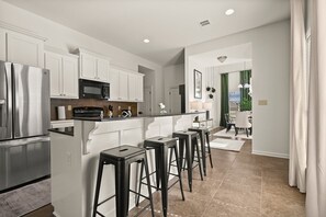 Una cocina moderna con gabinetes blancos, electrodomésticos de acero inoxidable y una barra con taburetes.