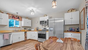 A modern kitchen with white cabinets, a wooden dining table, and stainless steel appliances. - Charming 3-bedroom cottage in serene Enumclaw with AC (Enumclaw)