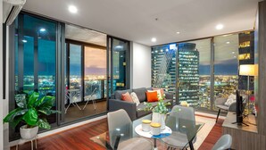 A modern living room with a glass table, chairs, a sofa, and a large window offering a city view.