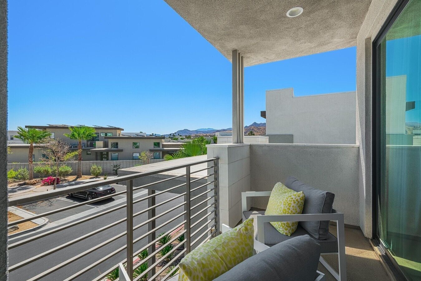 A balcony with a view of a street and buildings, a railing, and a seating area with cushions.