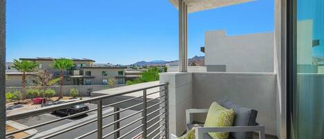 A balcony with a view of a street and buildings, a railing, and a seating area with cushions.
