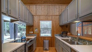 Una cocina compacta con paneles de madera, una ventana con persianas, electrodomésticos de acero inoxidable y un cubo de basura.