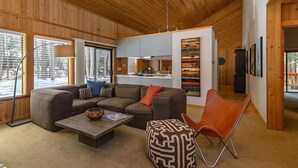 Una sala de estar acogedora con un sofá modular, una mesa de centro y un sillón de cuero. Se ve una cocina al fondo.