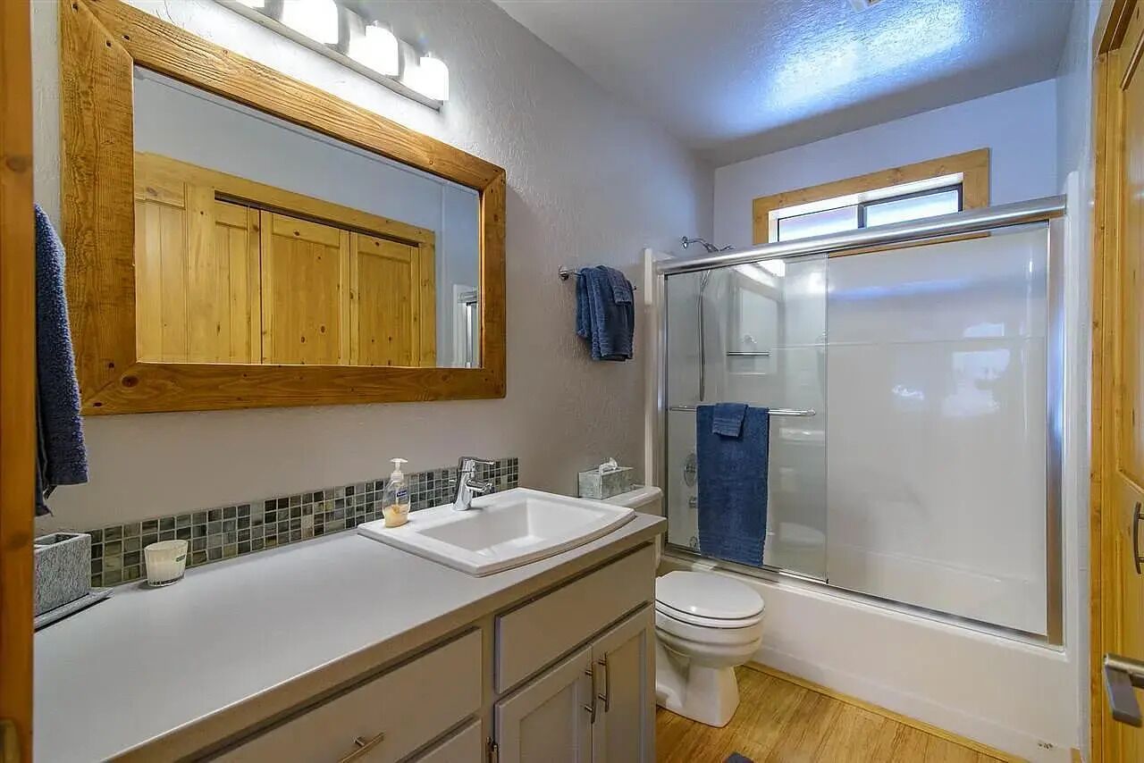 A bathroom with a wooden vanity, a white sink, a mirror, a glass shower enclosure, and a toilet.