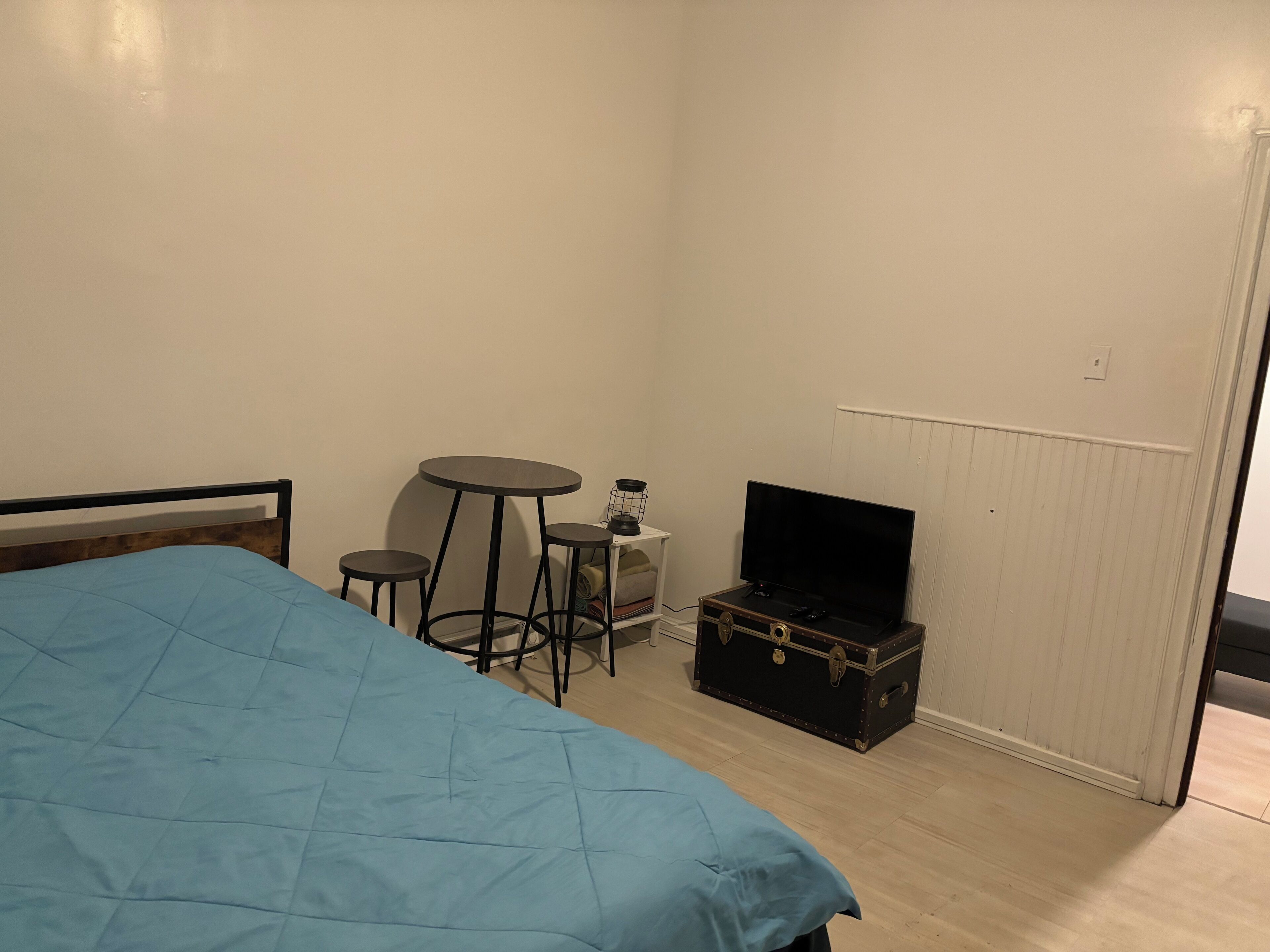 A bedroom with a bed, a small table, a television, and a suitcase.