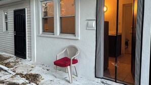 Talo, jossa on musta ovi, valkoinen tuoli punaisella koristetyynyllä ulkona, ja liukuovi, joka johtaa huoneeseen, jossa on laattalattia.