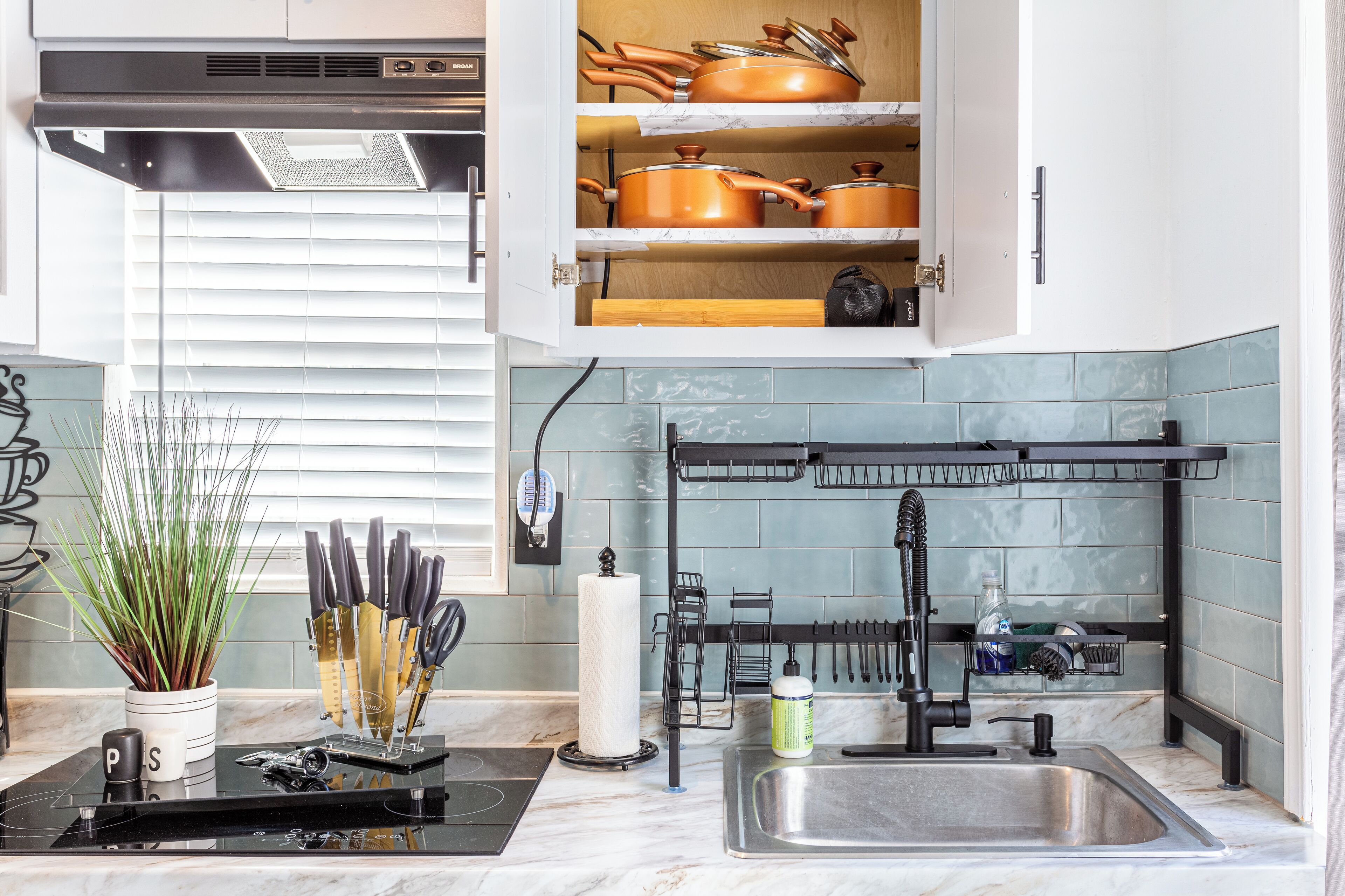 Una cocina moderna con horno empotrado, pileta de acero inoxidable y un colgador de ollas sobre la encimera.