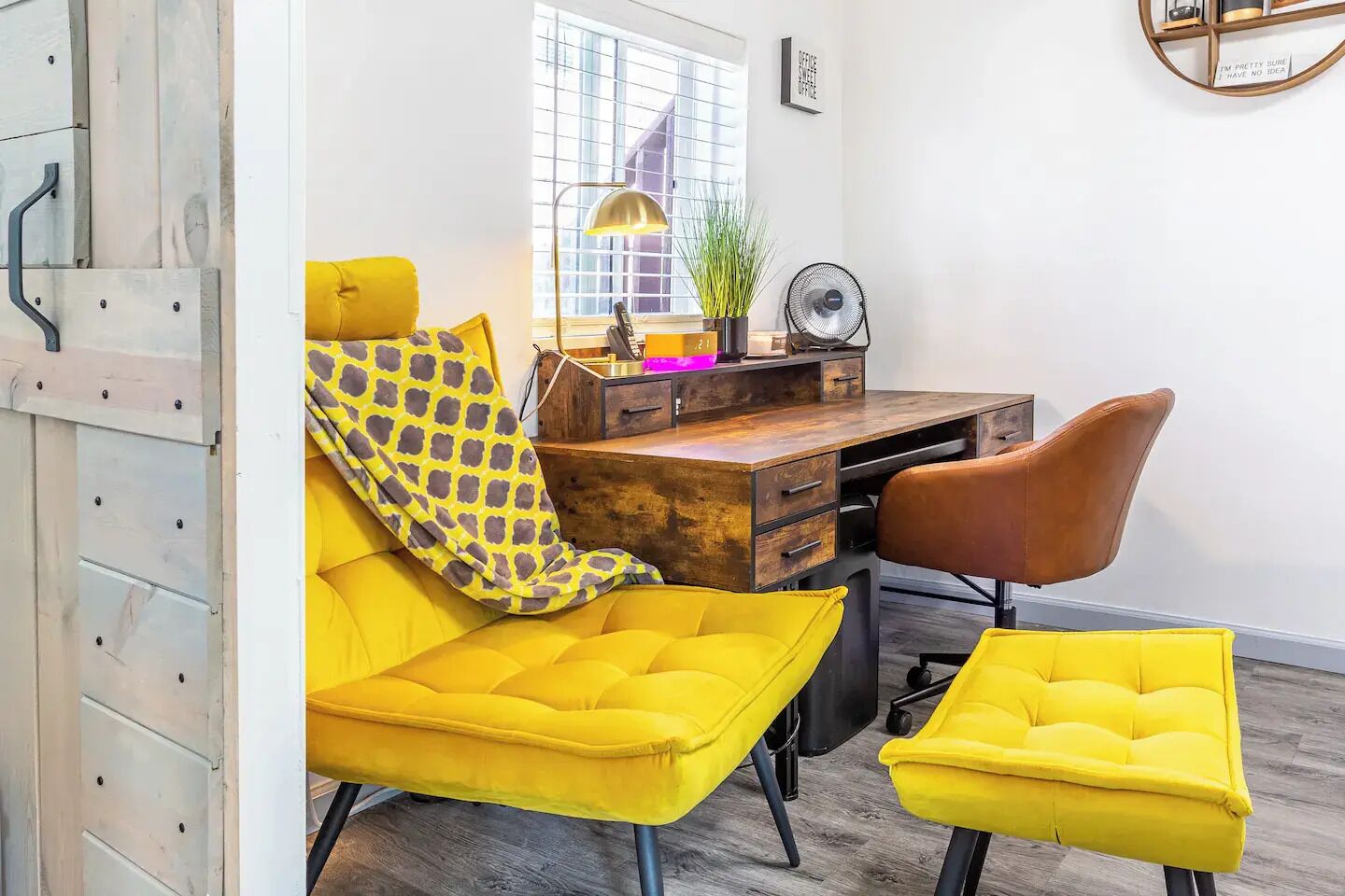 Un espacio de oficina moderno con un escritorio de madera, un sofá amarillo y un sillón de cuero marrón.