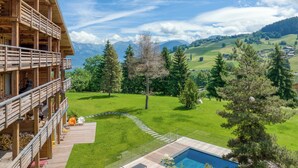A wooden chalet with a balcony overlooking a lush green landscape and a mountain range. - Appartement Élégance Mont Blanc - Welkeys (Combloux)
