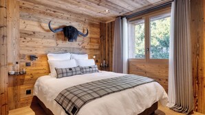 A wooden bedroom with a bed, pillows, and a mounted horn decoration. - Appartement Élégance Mont Blanc - Welkeys (Combloux)