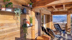 A wooden cabin interior with a wooden deck, chairs, and potted plants. - Appartement Élégance Mont Blanc - Welkeys (Combloux)