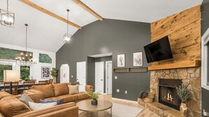 A modern living room with a stone fireplace, leather sofas, and a flat-screen TV mounted on a wooden wall.
