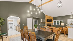 A spacious dining area with a dark wooden table and chairs, a chandelier, and a view into the kitchen.