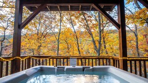 A hot tub with a wooden deck and railing, surrounded by autumn foliage.