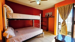 Et soveværelse med køjesenge, ventilator, lille bord og et vindue med gardiner.