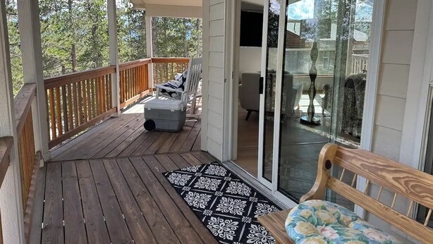A covered porch with a wooden deck, a bench, a cooler, and a patterned rug.