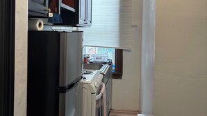 A compact kitchen with a refrigerator, stove, microwave, and a window with blinds. - Temple Hosp 2nd floor (Philadelphia)