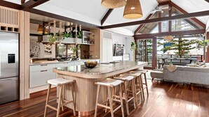 A modern kitchen with a central island, wooden bar stools, and a view of the outdoors. - Luxury On The Bay 2 - Ocean Views (Byron Bay)
