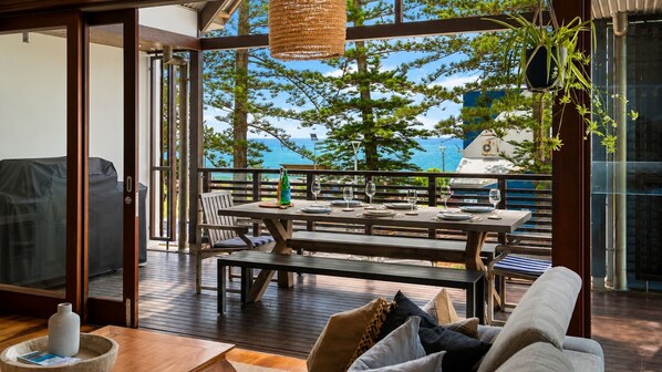 An outdoor dining area with a view of the sea, wooden furniture, and potted plants.